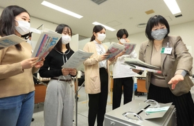 選挙管理委員会の職員（右）から投票所運営の手順を教わる神戸市外国語大の学生たち＝２３日午前、神戸市西区学園東町９