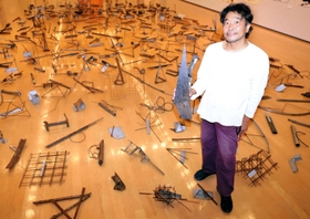 金属のさびや油汚れなどの風合いを生かした作品群。作品を手にする友井隆之さん＝兵庫県立美術館