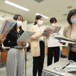 選挙管理委員会の職員（右）から投票所運営の手順を教わる神戸市外国語大の学生たち＝２３日午前、神戸市西区学園東町９