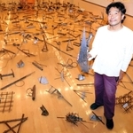 金属のさびや油汚れなどの風合いを生かした作品群。作品を手にする友井隆之さん＝兵庫県立美術館