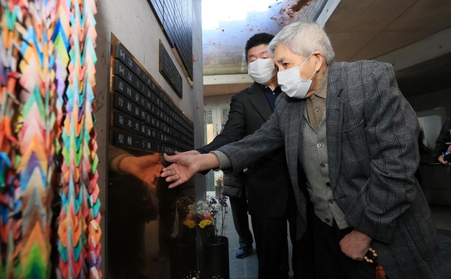 阪神・淡路大震災で妻を亡くして１９９６年に病死した父・田中秀市さんの名前が刻まれた銘板を貼り付ける、長男・田中正裕さん（手前）＝１１日午後、神戸市中央区加納町６（撮影・鈴木雅之）