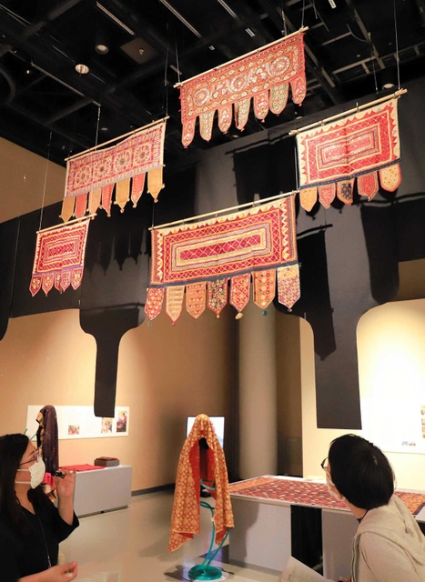 頭上には戸口飾りトーラン。金属入りのホースで作った人形に、婚礼用衣装などを掛ける斬新な展示も目を引く＝大阪府吹田市、国立民族学博物館