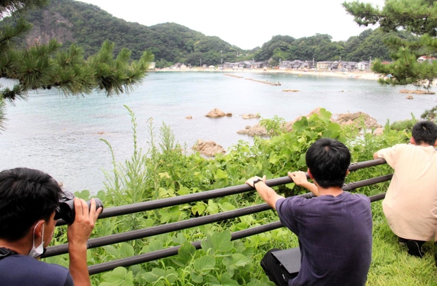 海水浴場近くの道路から密漁者を双眼鏡で監視する海上保安官＝８月、豊岡市竹野町切浜