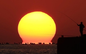だるま夕日が釣れました－。夕景に釣り人のシルエットが浮かんだ＝１０日午後４時４６分、明石市大久保町江井ケ島