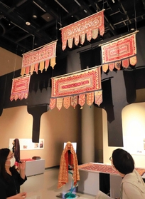 頭上には戸口飾りトーラン。金属入りのホースで作った人形に、婚礼用衣装などを掛ける斬新な展示も目を引く＝大阪府吹田市、国立民族学博物館