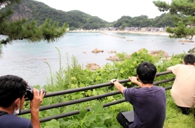 海水浴場近くの道路から密漁者を双眼鏡で監視する海上保安官＝８月、豊岡市竹野町切浜