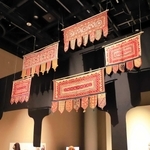 頭上には戸口飾りトーラン。金属入りのホースで作った人形に、婚礼用衣装などを掛ける斬新な展示も目を引く＝大阪府吹田市、国立民族学博物館