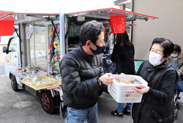 なじみになった客から買い物かごを受け取る「とくし丸」販売員の野崎敏郎さん＝淡路市江井