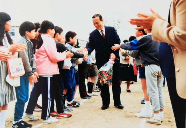 小山健治さんの父晃一さん（中央）。小学校教諭として児童たちに笑顔で見送られる様子の写真が残る（健治さん提供）