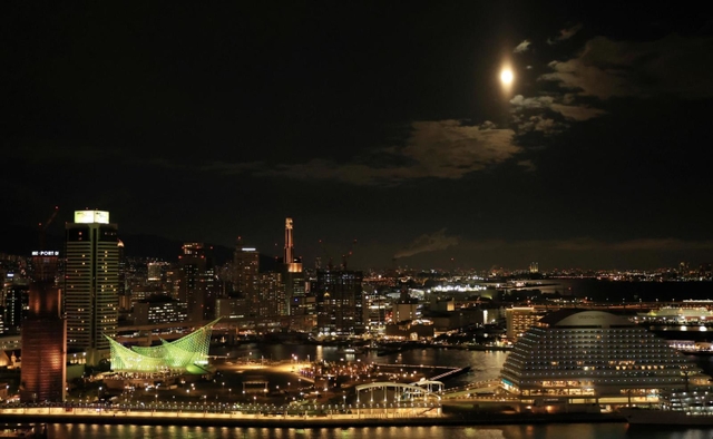 ２０２２年で地球から最も遠く小さく見える満月「ミニマムムーン」。神戸港の夜景と共演も、小さめの主役？＝１８日午後６時２７分、神戸市中央区東川崎町１、神戸新聞社から（撮影・鈴木雅之）