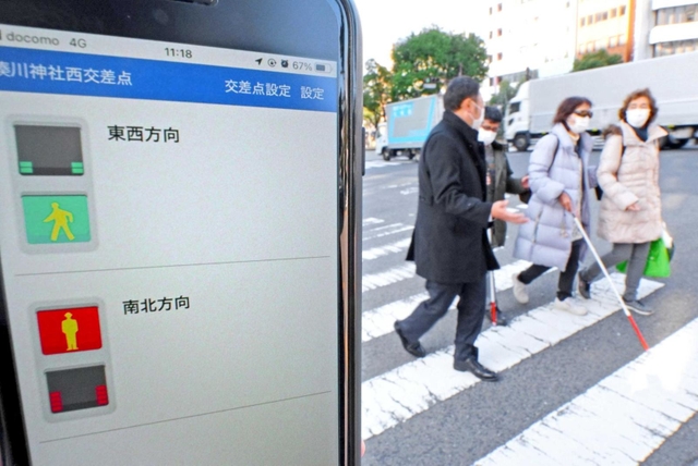 スマートフォンアプリ「信ＧＯ！」の画面と、アプリを利用して横断歩道を渡る視覚障害者ら＝神戸市中央区