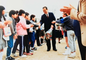 小山健治さんの父晃一さん（中央）。小学校教諭として児童たちに笑顔で見送られる様子の写真が残る（健治さん提供）