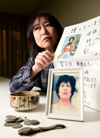 母正子さんのちらしを手にする佐藤悦子さん。手前は母の写真と焼け跡から見つかった腕時計や小銭＝加古川市内（撮影・中西幸大）
