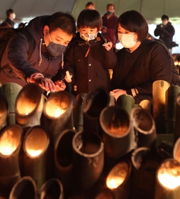 亡くなった祖父の慰霊のため東遊園地を訪れた大前敏郎さん（左）。竹灯ろうに明かりをともしながら長男に祖父のことを話して聞かせた＝１７日午後、神戸市中央区加納町６（撮影・小林良多）