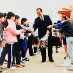 小山健治さんの父晃一さん（中央）。小学校教諭として児童たちに笑顔で見送られる様子の写真が残る（健治さん提供）