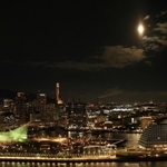 ２０２２年で地球から最も遠く小さく見える満月「ミニマムムーン」。神戸港の夜景と共演も、小さめの主役？＝１８日午後６時２７分、神戸市中央区東川崎町１、神戸新聞社から（撮影・鈴木雅之）