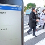 スマートフォンアプリ「信ＧＯ！」の画面と、アプリを利用して横断歩道を渡る視覚障害者ら＝神戸市中央区