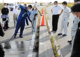 除草方法のアイデアコンテストで、道路脇の雑草に熱湯をかけていく参加者＝昨年１０月、尼崎市内（県西宮土木事務所提供）