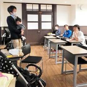 長女を抱きながら「働き方」の授業をする灘高校の片田孫朝日教諭（左）＝神戸市東灘区魚崎北町８（本人提供）
