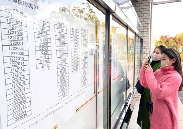 合格を確認し、張り出された番号を写真撮影する受験生と保護者＝７日午前、神戸市西区学園東町９、神戸市外国語大学（撮影・坂井萌香）