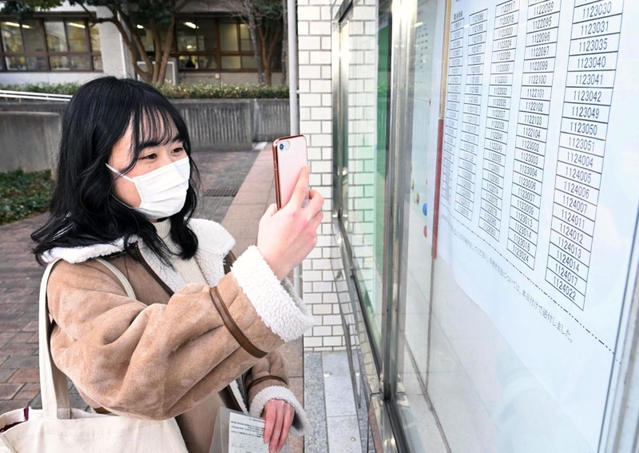合格を確認し、張り出された番号を写真撮影する受験生＝７日午前、神戸市西区学園東町９、神戸市外国語大学（撮影・坂井萌香）