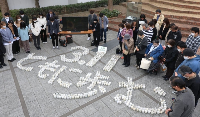 「３・１１　ともに歩む」の文字の形に並べたろうそくを囲み、黙とうをささげる参加者＝１１日午後２時４６分、神戸市中央区加納町６（撮影・吉田敦史）