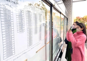 合格を確認し、張り出された番号を写真撮影する受験生と保護者＝７日午前、神戸市西区学園東町９、神戸市外国語大学（撮影・坂井萌香）