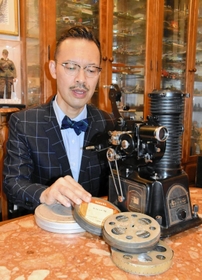岡部芳郎さんの数少ない遺品である映写機とフィルムを手に、足跡を語る孫の芳彦さん＝神戸市灘区