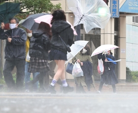 暴風雨の中、傘を飛ばされそうになりながら歩く人たち＝１８日午後、神戸市中央区東川崎町１