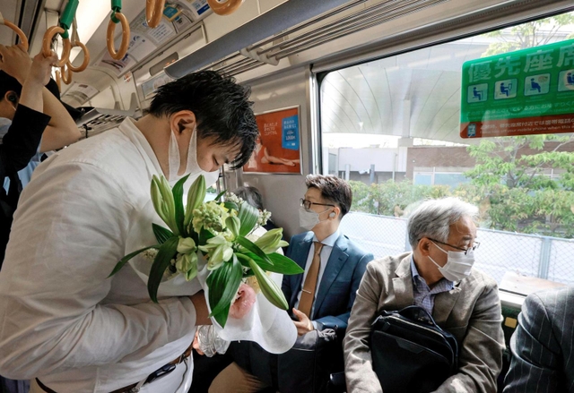 尼崎ＪＲ脱線事故から１７年となり、現場付近を走行する電車内で、花を手に目を閉じる乗客＝２５日午前９時１６分、尼崎市（代表撮影）