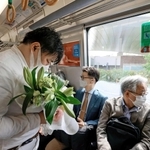 尼崎ＪＲ脱線事故から１７年となり、現場付近を走行する電車内で、花を手に目を閉じる乗客＝２５日午前９時１６分、尼崎市（代表撮影）