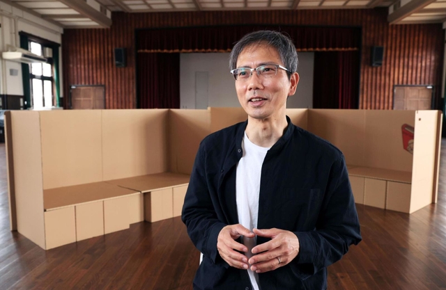 震災学習で使う段ボールベッドの前で、１万日の歩みを振り返る山住勝利さん＝神戸市長田区二葉町７、ふたば学舎講堂（撮影・鈴木雅之）