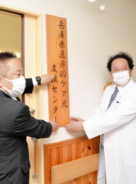 兵庫県医療的ケア児支援センターの看板を掲げる常石秀市・医療福祉センターきずな院長（右）と生安衛・県福祉部長＝加西市若井町