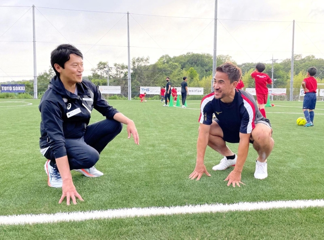 環境に配慮した人工芝の感触を確かめながら、斎藤元彦知事（左）と笑顔で話す岡崎慎司選手＝神戸市西区平野町印路