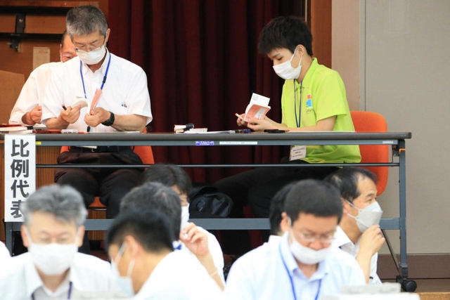 集計された投票用紙の束を確認する開票立会人。２４歳の介護士武田詩音さん（右奥）は「投じられた票に触れることで、その重みを実感した」＝１０日午後１１時２４分、猪名川町紫合