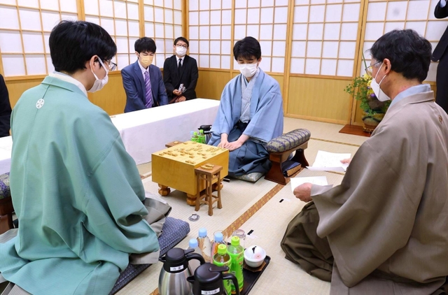 立会人の深浦康市九段（右）から封じ手を示される藤井聡太王位（中央）。左は豊島将之九段＝１４日午前、札幌市南区、ぬくもりの宿ふる川
