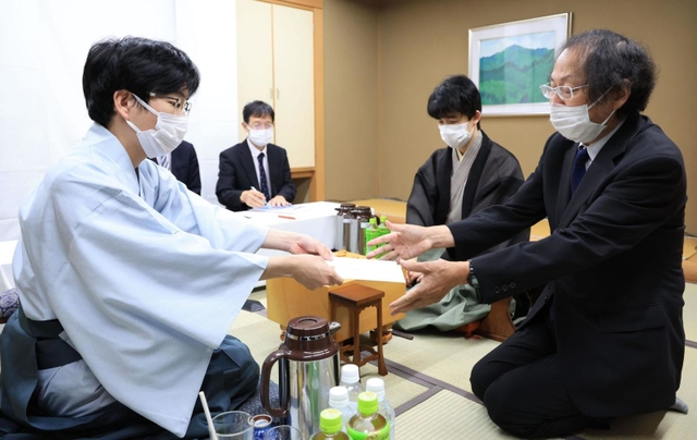 立会人の福崎文吾九段（右）に封じ手を渡す豊島将之九段（左）。右奥は藤井聡太王位＝２０日午後６時１２分、神戸市北区有馬町、有馬温泉の旅館「中の坊瑞苑」（撮影・吉田敦史）