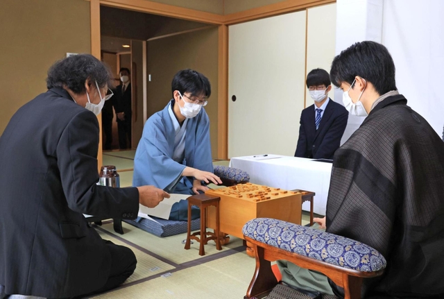 「お～いお茶杯第６３期王位戦」７番勝負の第３局で、立会人の福崎文吾九段（左）から封じ手を示される藤井聡太王位（右）。奥は豊島将之九段＝２１日午前、神戸市北区有馬町、有馬温泉の旅館「中の坊瑞苑」（撮影・鈴木雅之）