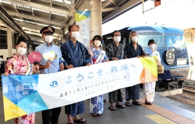 城崎温泉駅を出発する銀河の前で撮影する城崎温泉観光大使や登日幸治但馬県民局長（右から２人目）＝１日午後、豊岡市城崎町、ＪＲ城崎温泉駅