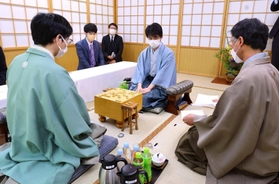 立会人の深浦康市九段（右）から封じ手を示される藤井聡太王位（中央）。左は豊島将之九段＝１４日午前、札幌市南区、ぬくもりの宿ふる川