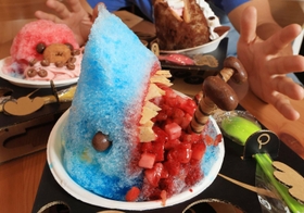 人の脚に見立てた棒状の菓子を差した「サメ氷　被害者つき」。口の中の赤はイチゴの果肉で表現した＝神戸市須磨区行幸町３、カフェ「パパパピッピーズ」（撮影・吉田敦史）