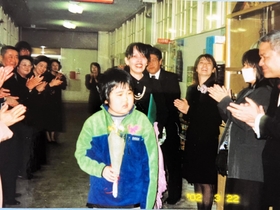 重病を乗り越え、鶴甲小学校の卒業式に臨む市川裕太さんと母玲子さん。先生や職員が祝福する＝２００２年、神戸市灘区（市川さん提供）