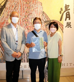 来場１万人目となり、石井嘉彦副館長（左）から記念品を贈られた永田敏彦さんと由美子さん夫婦＝神戸市東灘区向洋町中２
