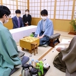 立会人の深浦康市九段（右）から封じ手を示される藤井聡太王位（中央）。左は豊島将之九段＝１４日午前、札幌市南区、ぬくもりの宿ふる川