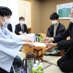 立会人の福崎文吾九段（右）に封じ手を渡す豊島将之九段（左）。右奥は藤井聡太王位＝２０日午後６時１２分、神戸市北区有馬町、有馬温泉の旅館「中の坊瑞苑」（撮影・吉田敦史）