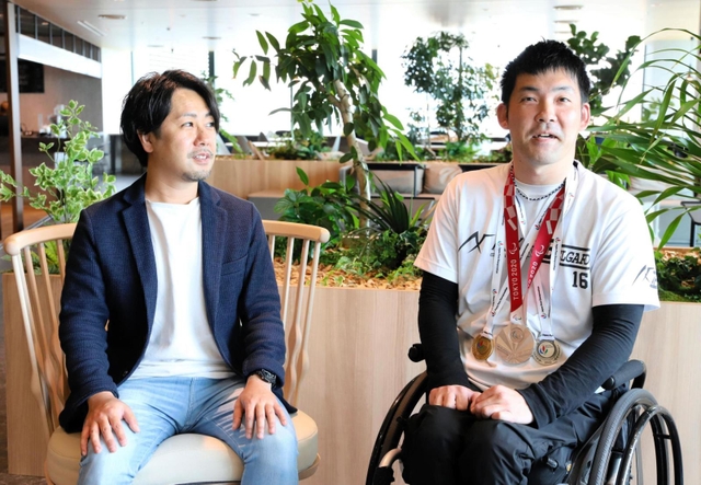 東京パラリンピックの銀メダルなどを首に掛け、Ｄ２Ｃのグループ本社を訪れた大矢勇気（右）。隣が採用を担当した青沼邦之さん＝５月１８日、東京都港区（同社提供）