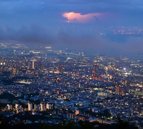 薄暮の中で輝く神戸の街。大阪方面の空では稲妻がまばゆい光を放っていた＝１６日夜、神戸市灘区摩耶山町、掬星台（撮影・秋山亮太）