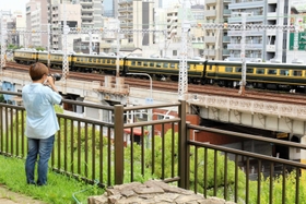 ＪＲ神戸線を走るのは数年ぶりという「サロンカーなにわ」を花隈公園から撮影する男子大学生。三宮のビル群を構図に取り込めるので、お気に入りの撮影スポットだという＝神戸市中央区花隈町