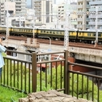 ＪＲ神戸線を走るのは数年ぶりという「サロンカーなにわ」を花隈公園から撮影する男子大学生。三宮のビル群を構図に取り込めるので、お気に入りの撮影スポットだという＝神戸市中央区花隈町