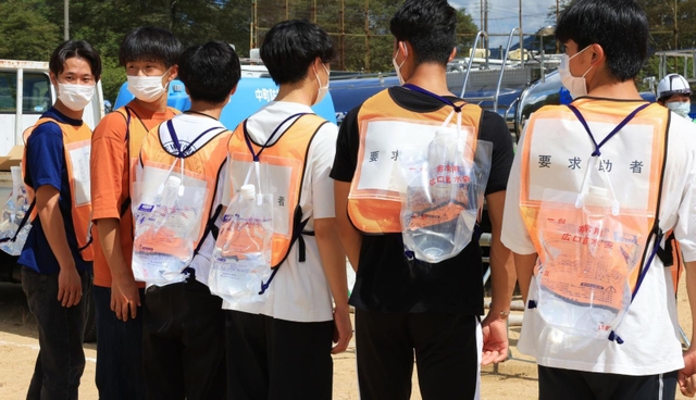 訓練でリュック型の給水袋を背負った負傷者役の大学生ら＝４日午前、兵庫県多可町中区岸上、町立中央公園（撮影・鈴木雅之）